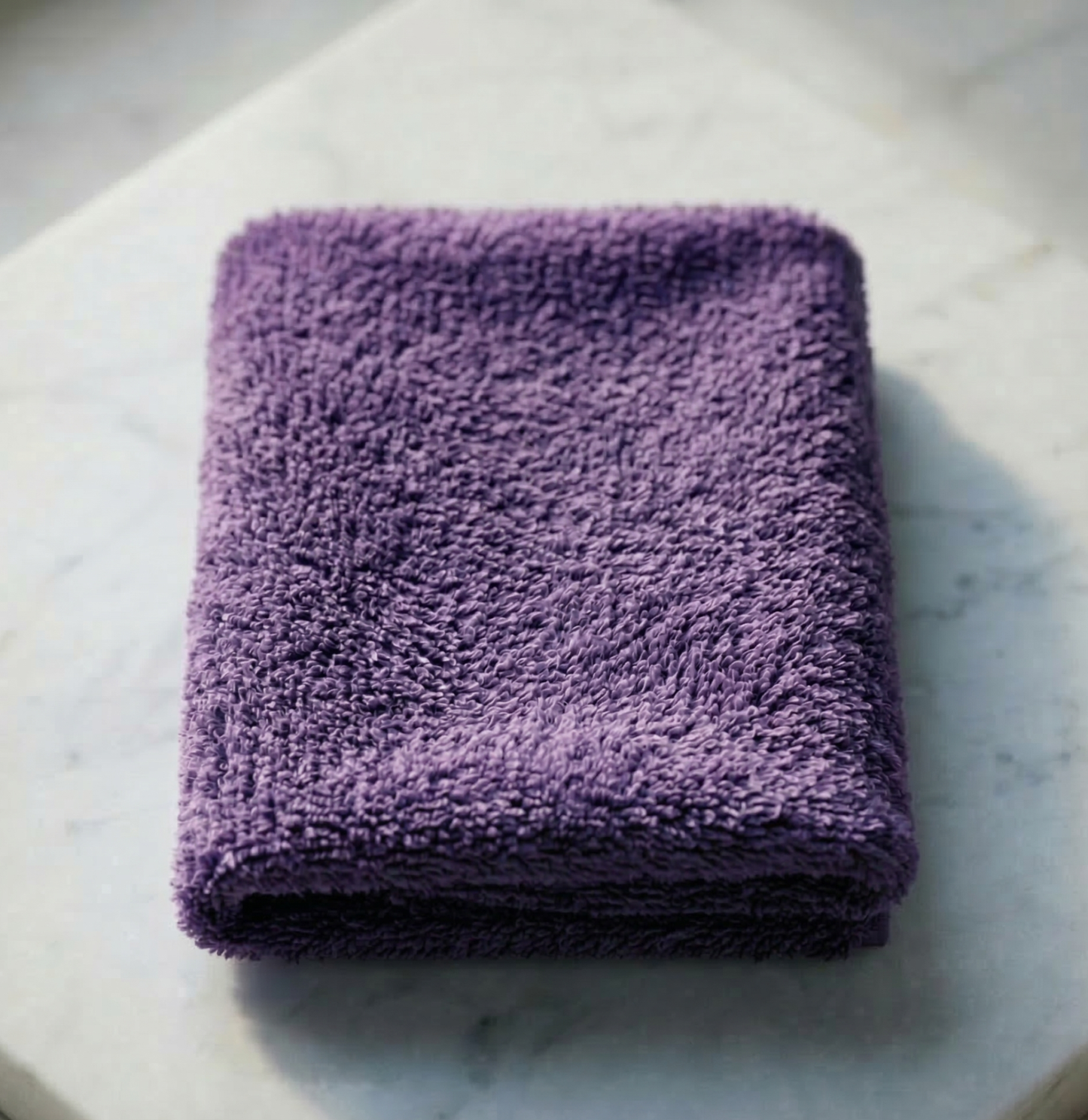 A neatly folded vibrant violet EXLUX premium skincare facial towel displaying its plush microfiber texture on a white marble surface