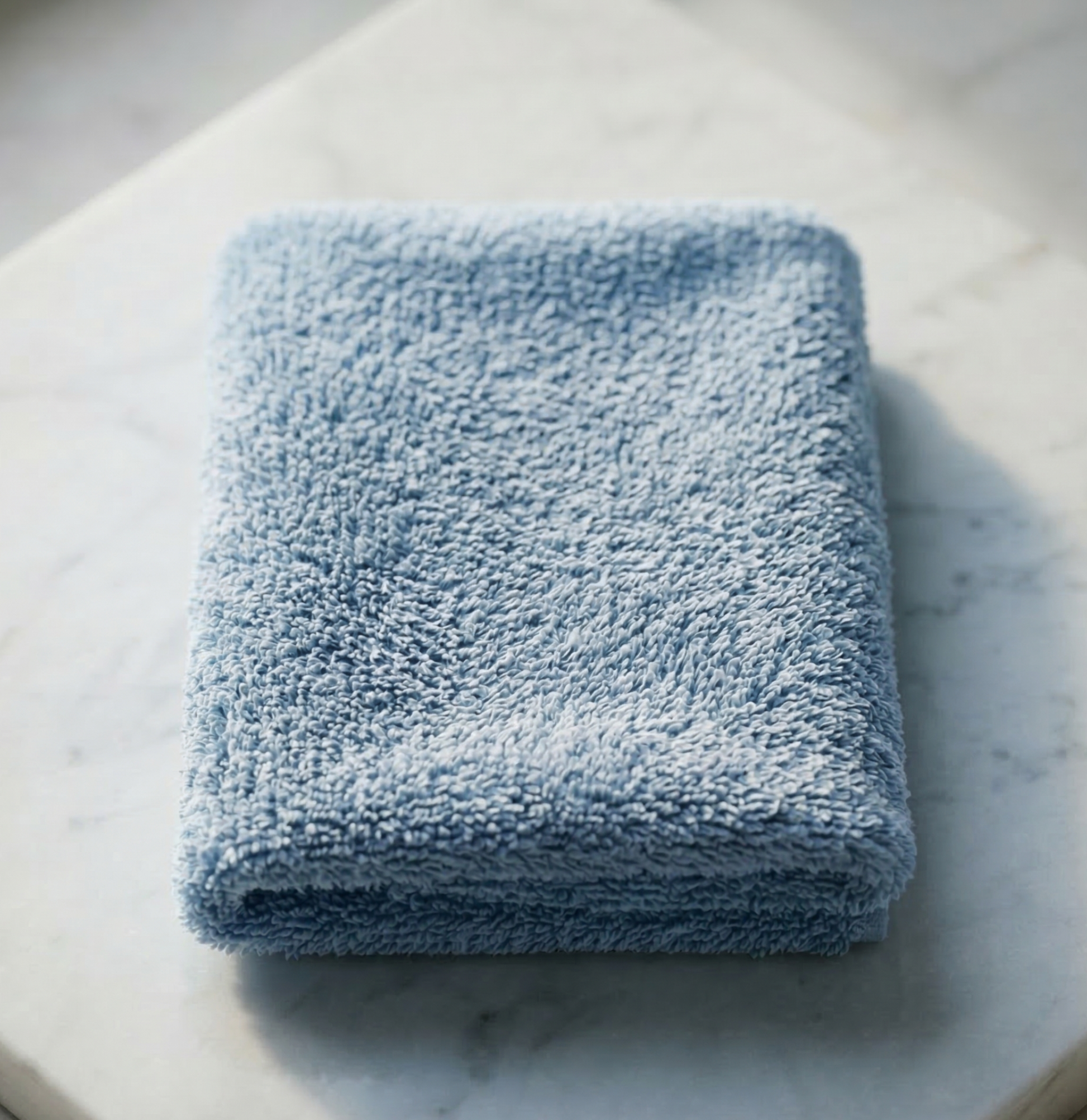 A neatly folded light blue EXLUX premium skincare facial towel displaying its plush microfiber texture on a white marble surface