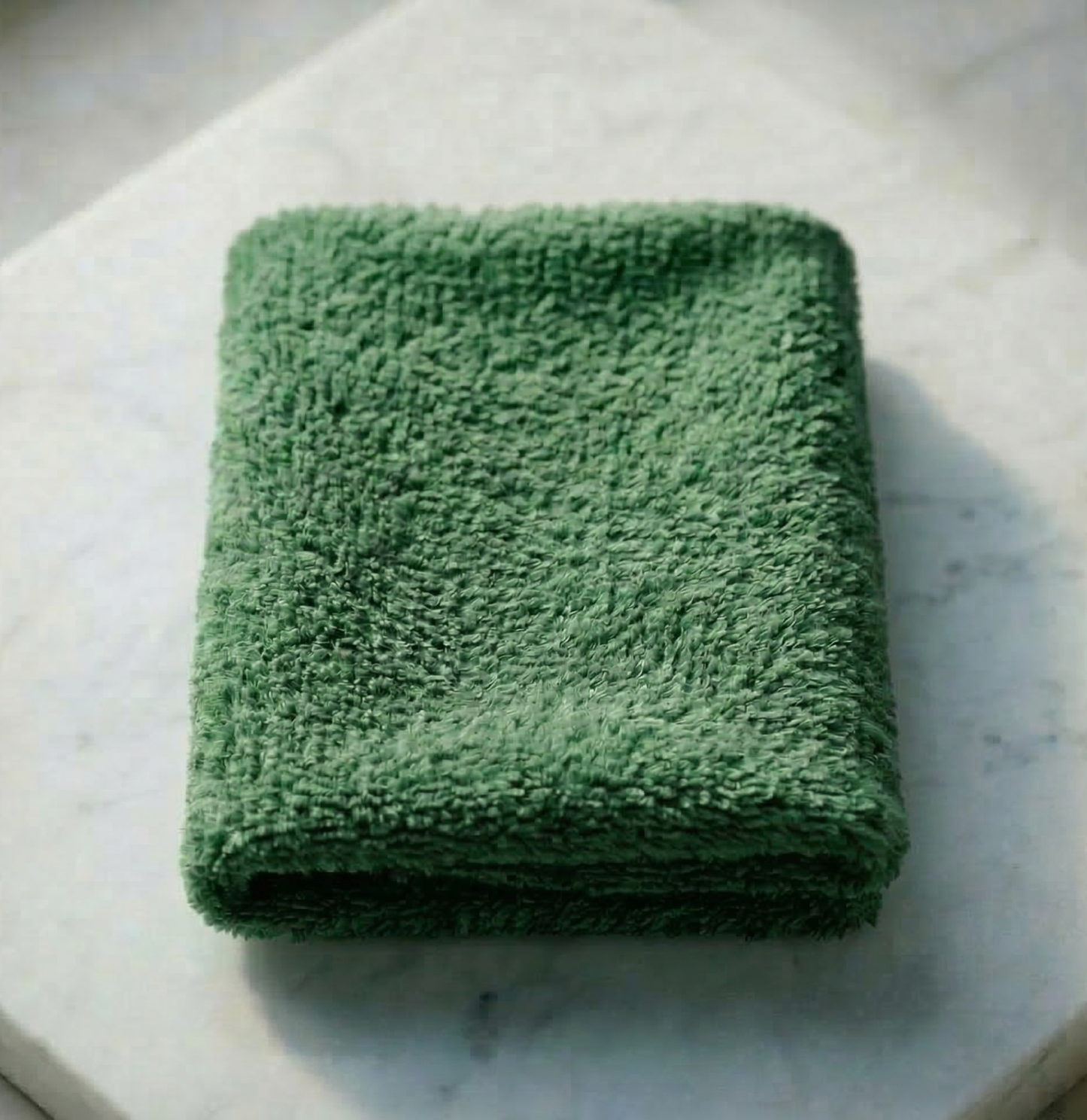 A neatly folded emerald green EXLUX premium skincare facial towel displaying its plush microfiber texture on a white marble surface