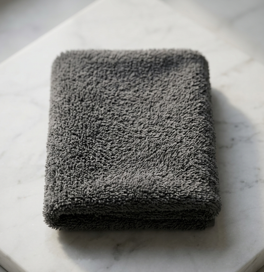 A neatly folded stone grey EXLUX premium skincare facial towel displaying its plush microfiber texture on a white marble surface