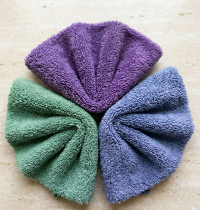 A stack of two folded EXLUX premium skincare facial towels in bright yellow and stone grey displaying their plush microfiber texture on a white marble surface