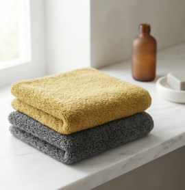 A neatly folded stone grey EXLUX premium skincare facial towel displaying its plush microfiber texture on a white marble surface