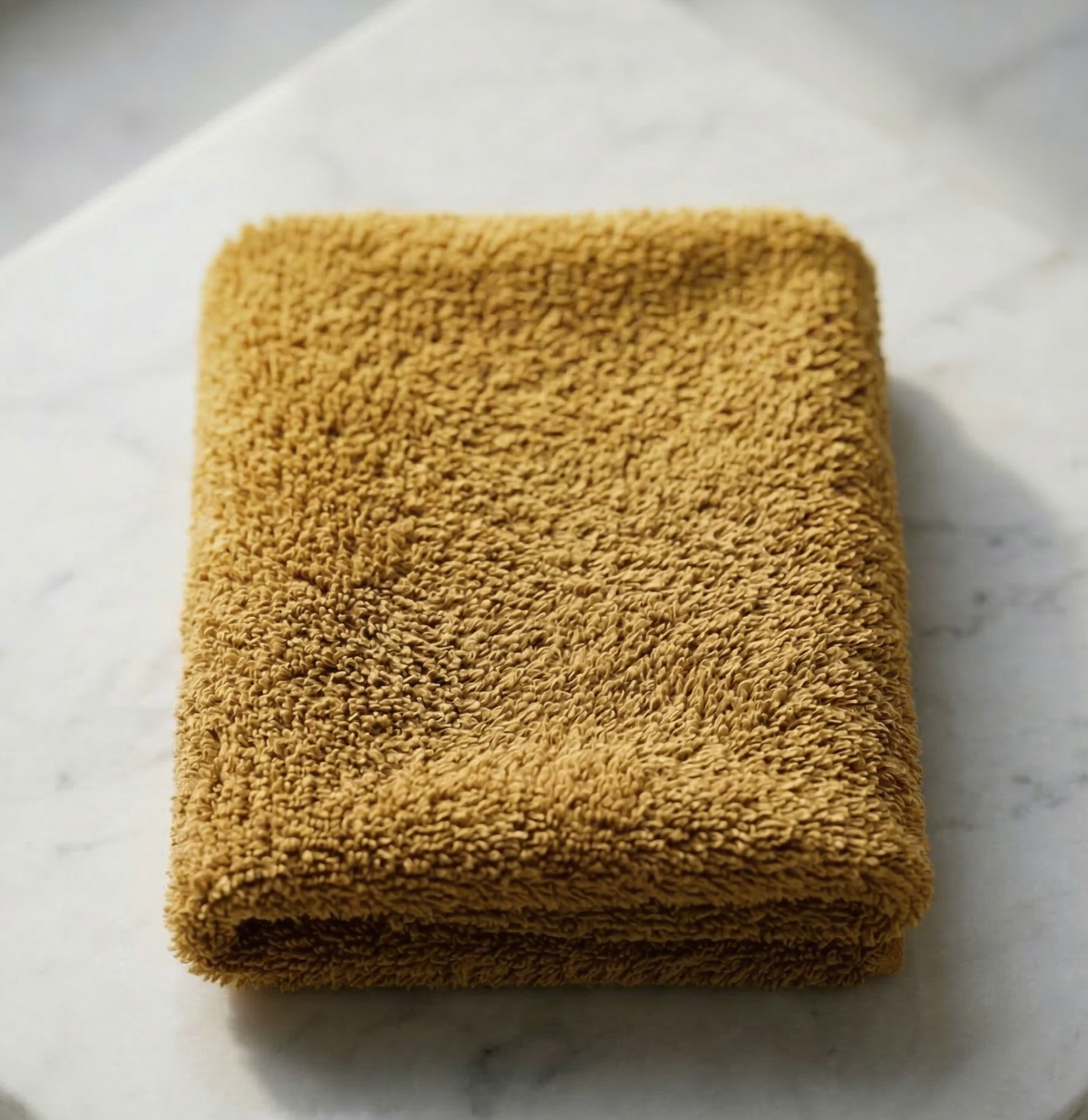 A neatly folded bright mustard yellow EXLUX premium skincare facial towel displaying its plush microfiber texture on a white marble surface